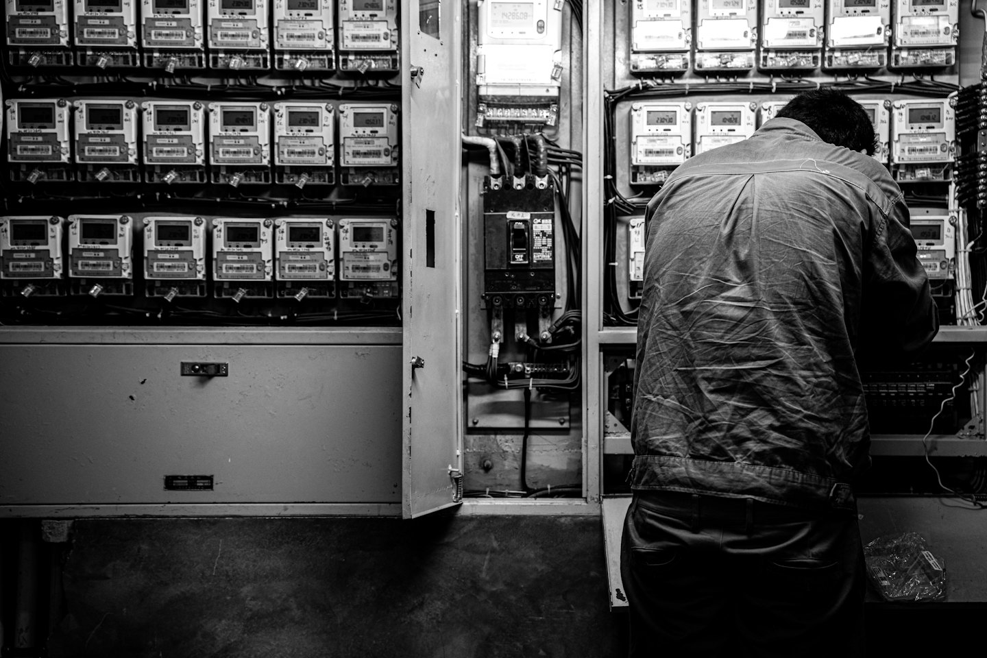 Karmaşık kablolarla açık bir elektrik panosunda çalışan kişi.